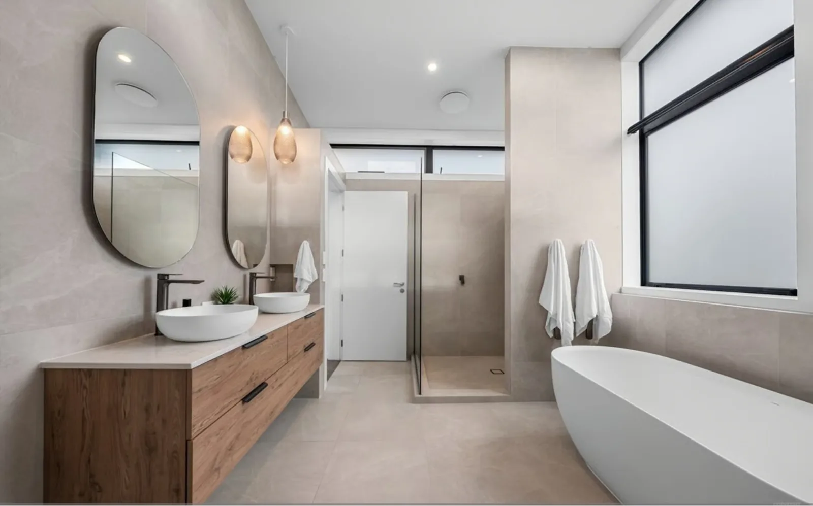 A completed bathroom renovation with twin basins on a timber vanity and a freestanding bath under the window
