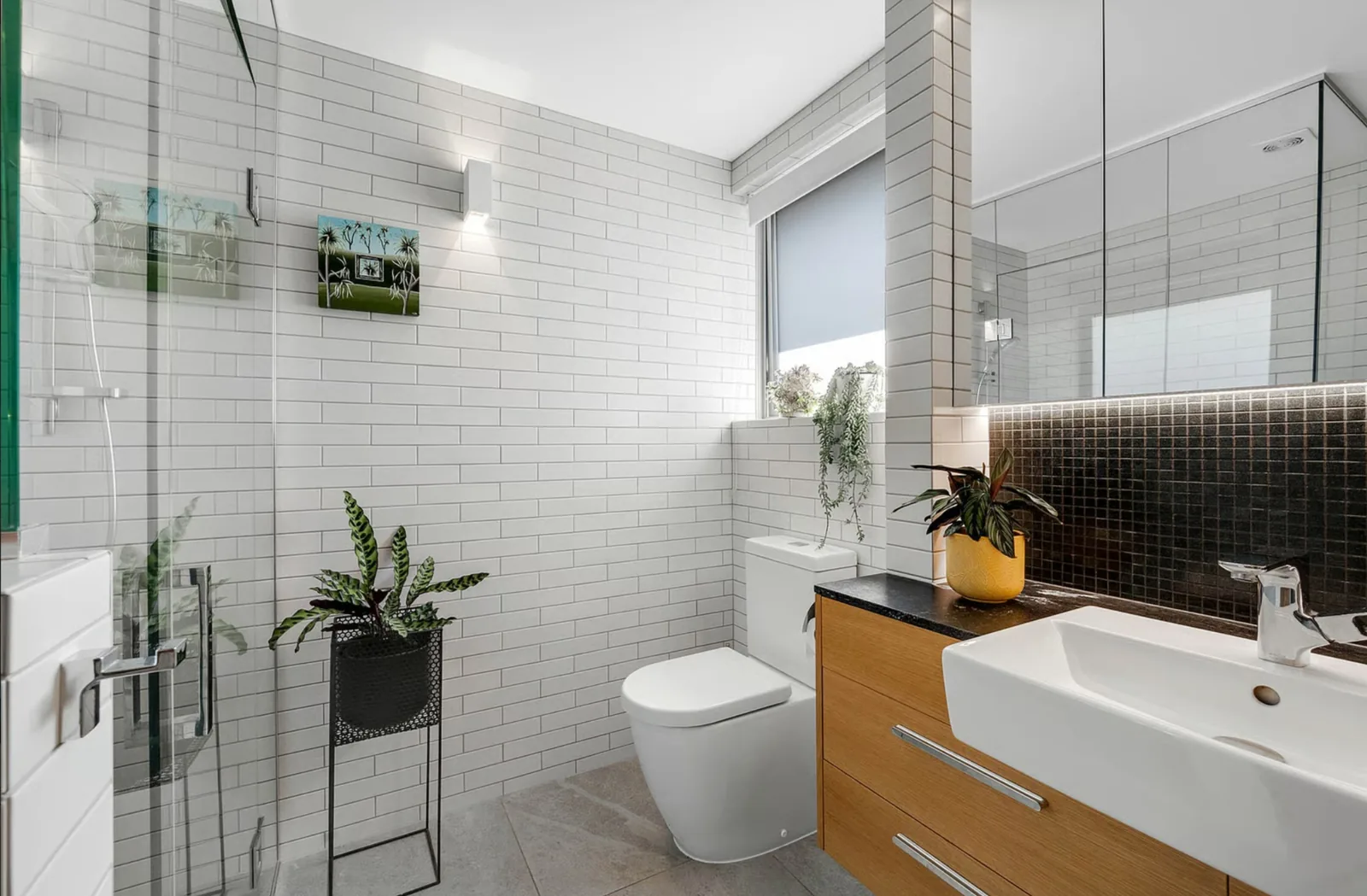 A completed bathroom renovation tiled in white subway with a timber vanity and a dark mosaic splashback