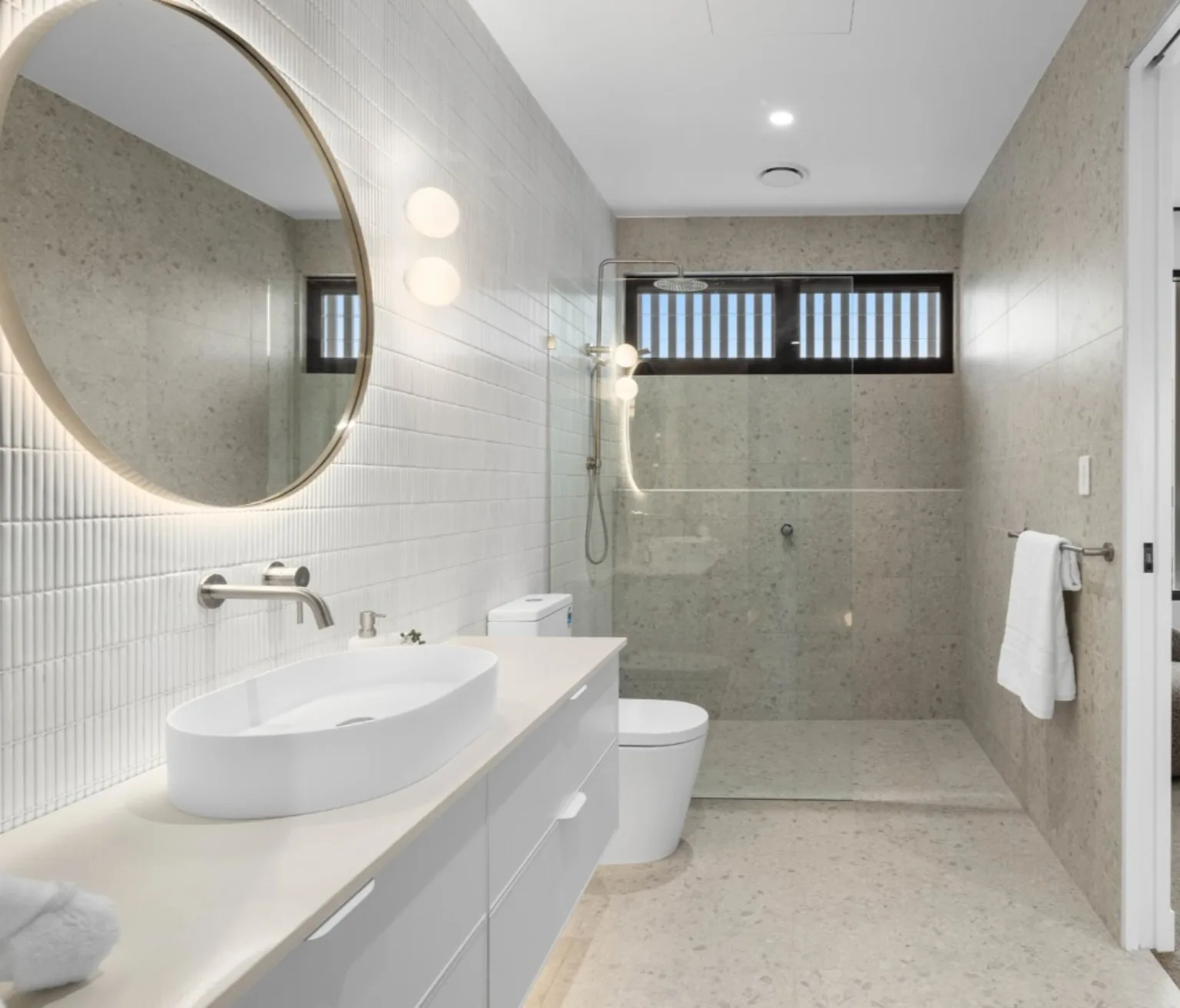 A completed bathroom renovation with a walk in shower behind frameless glass and a round backlit mirror over the vanity