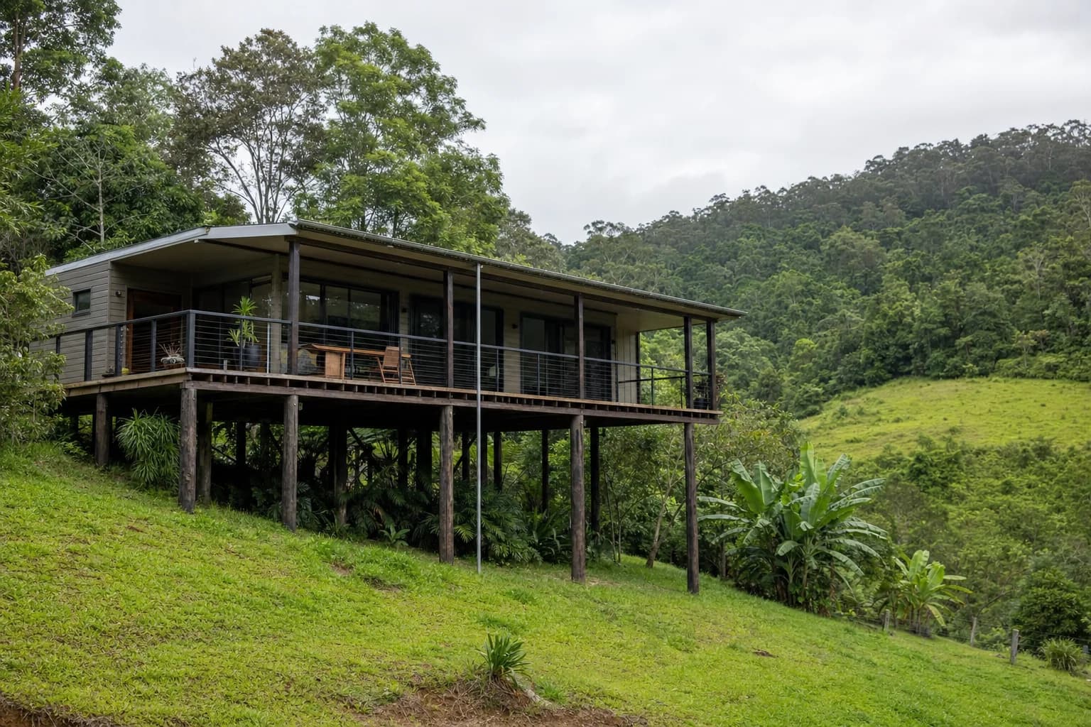 A timber pole home standing on a steep green slope in the Federal hinterland