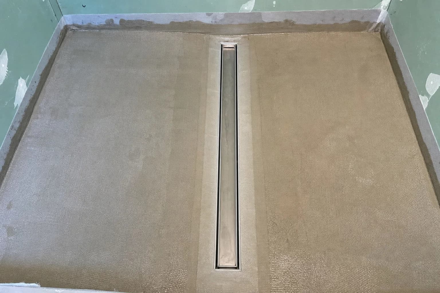 A long strip drain bedded into the floor with the waterproofing carried over it
